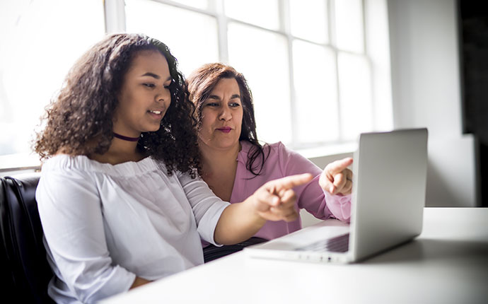 A teacher and student pointing to a laptop screen