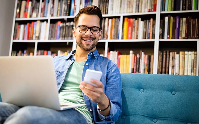 Student with a laptop and smartphone with a wall of books in the background