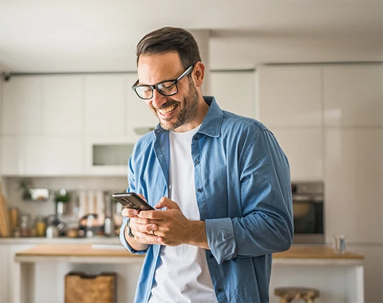 A smiling man in his kitchen using his cellphone